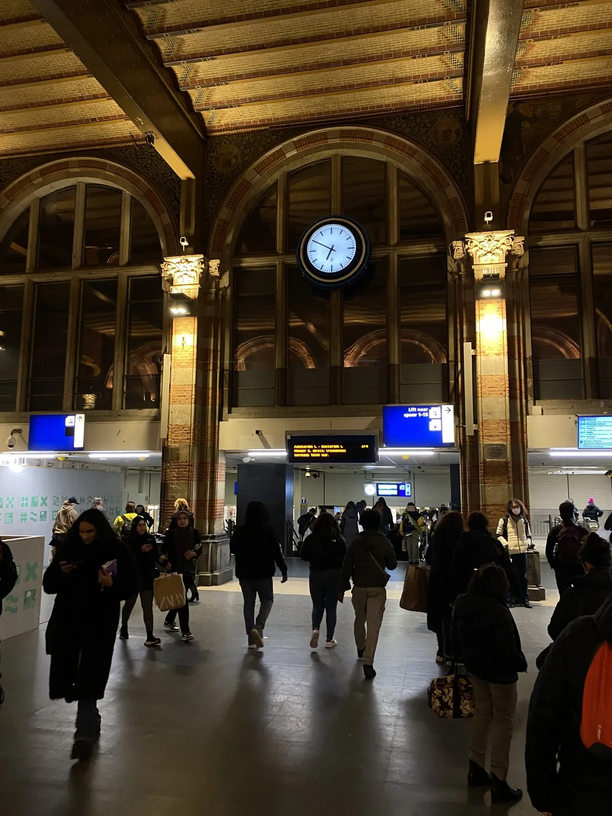 A round modern clock, placed perfectly inside an arch of an old train station. It points at ten minutes to seven.