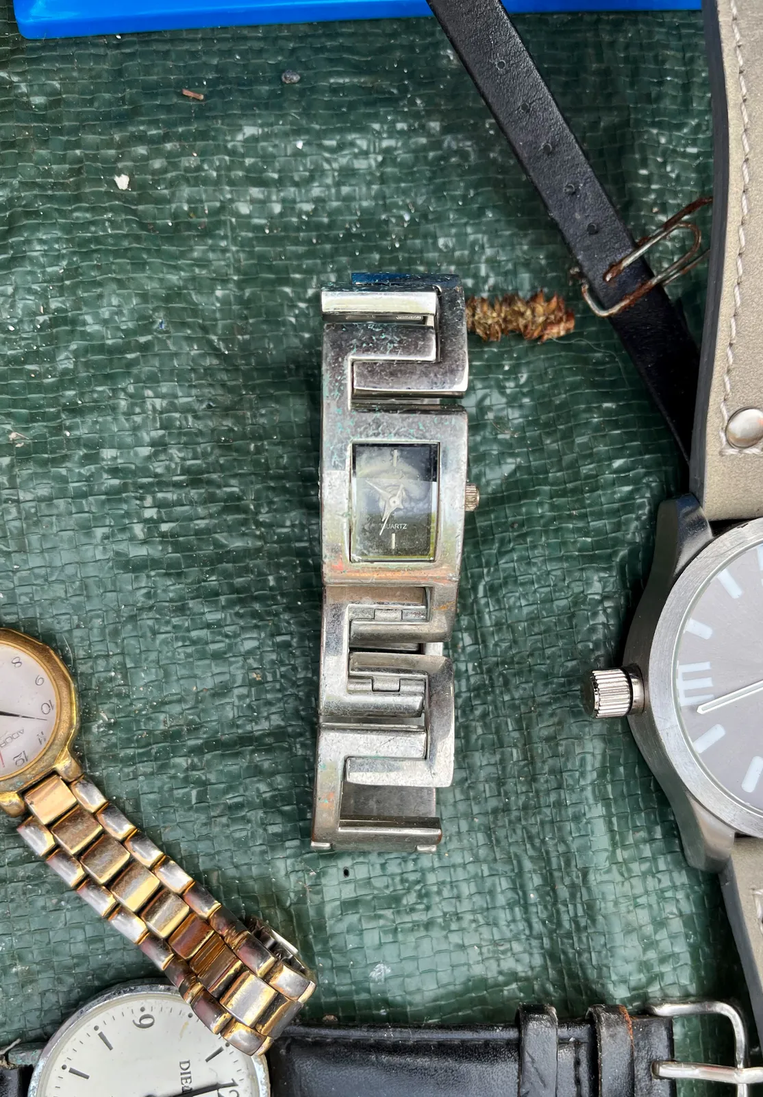 A silvery looking watch, with a square face, points at 10 minutes to seven.