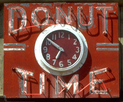 This clock points at nine minutes to seven. The words, in neon, around it say Donut Time.