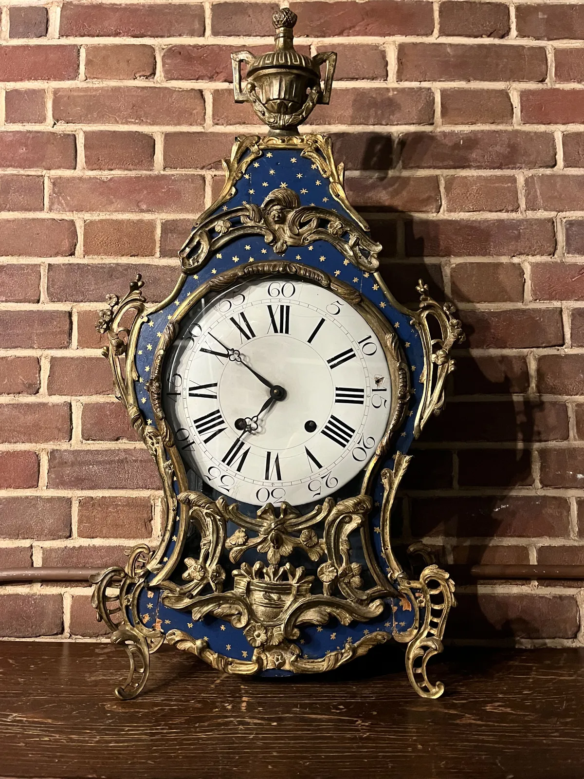 An old, mantel clock, richly decorated with metal ornaments and blue parts with stars. The clock points at 9 minutes to 7.