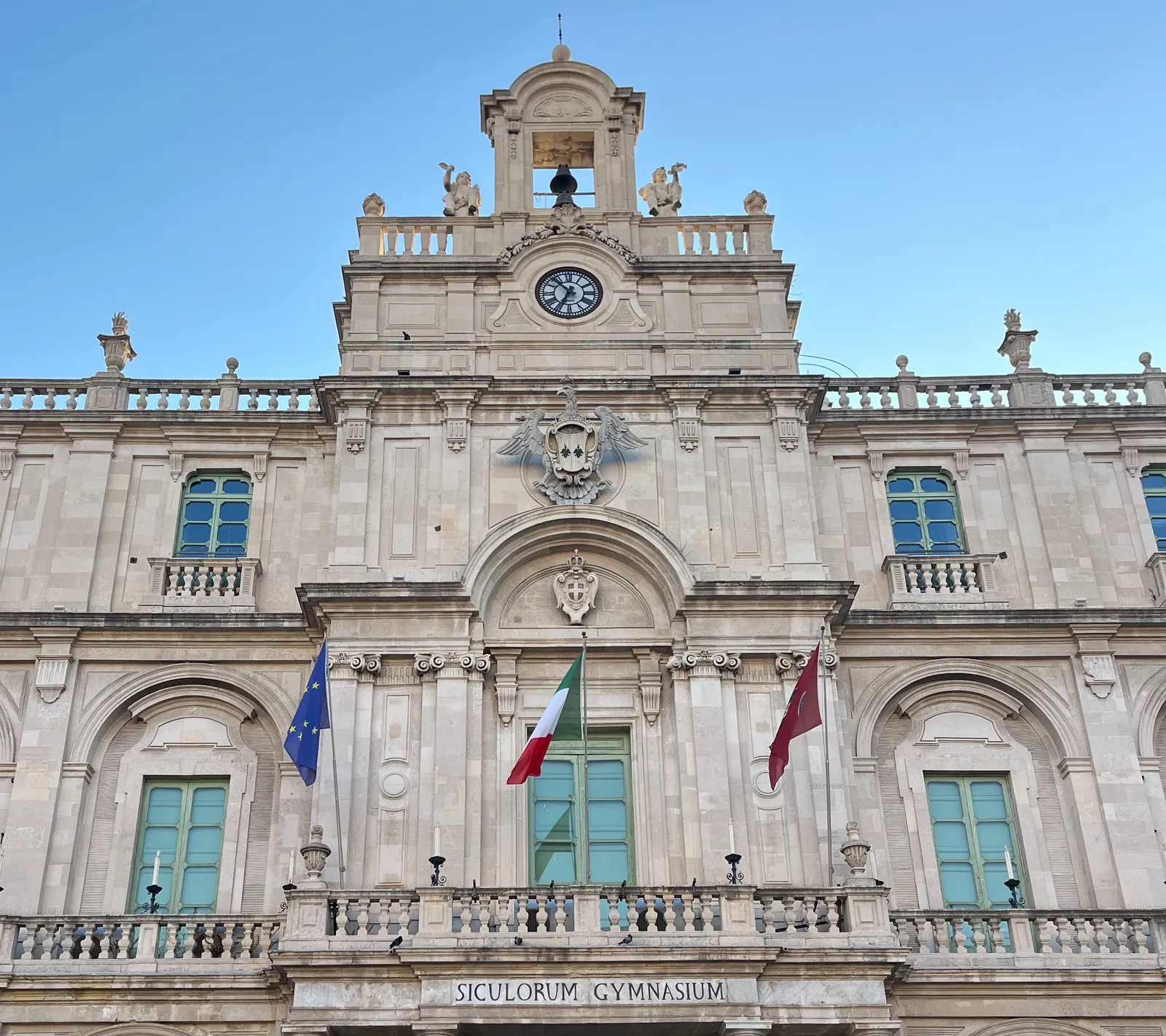 The facade of the Siculorum Gymnasium, which means Sicilian Gymnasium, there’s a clock that points at 7 minutes to 7.