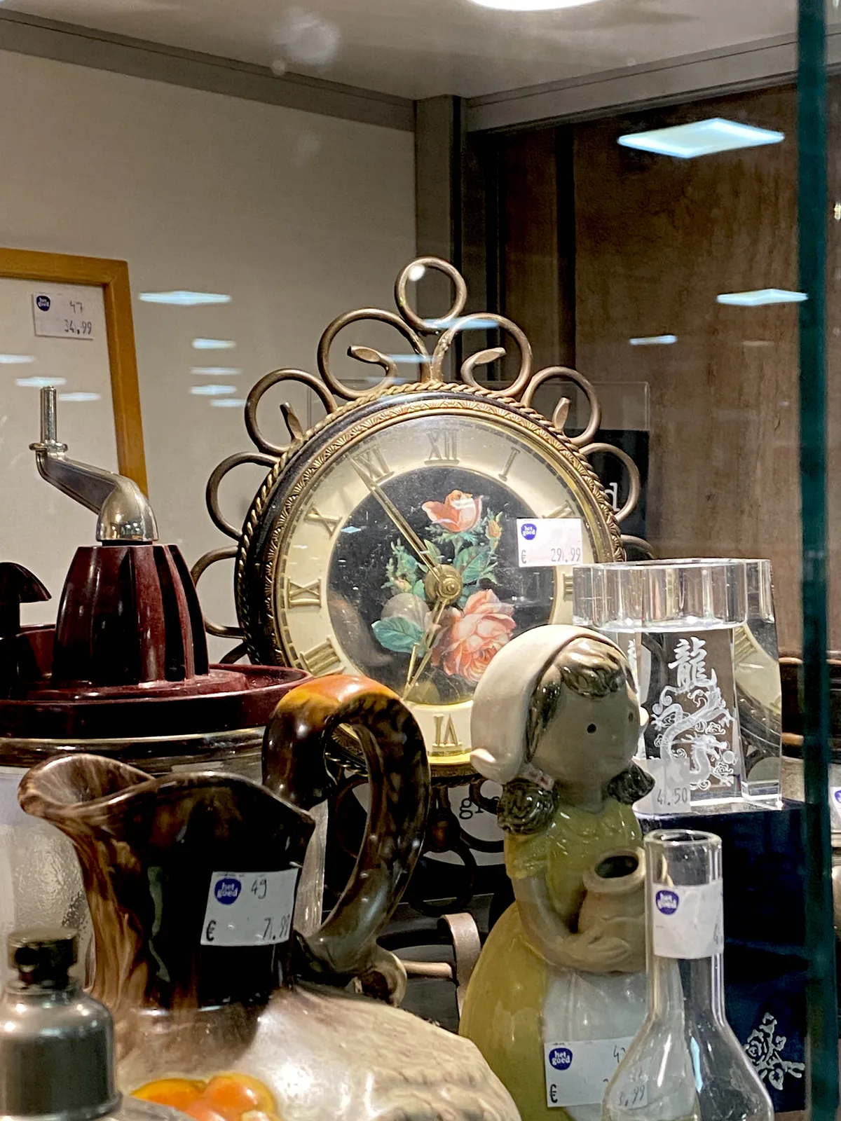Lots of stuff for sale in this thrift shop. Among the stuff there’s an ornamented clock. It points at 6 minutes to 7.