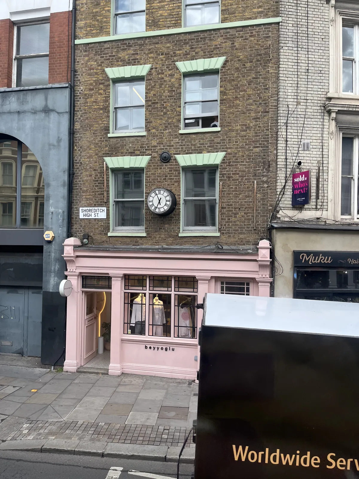 A clock on the facade of a shop on Shoreditch High Street. A delivery truck is parked in front of it. The clock points at 4 minutes to six.