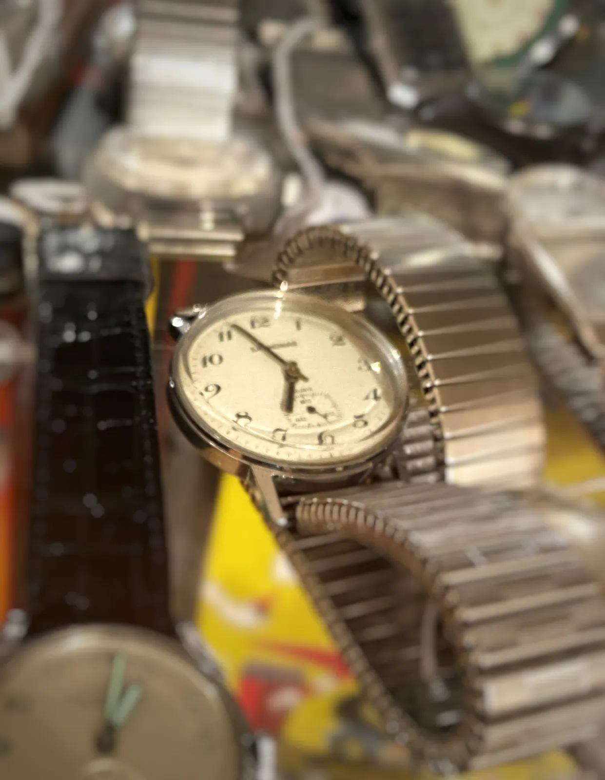 Many old watches, all together. One of them is in focus and it points at It is 3 minutes to 7.