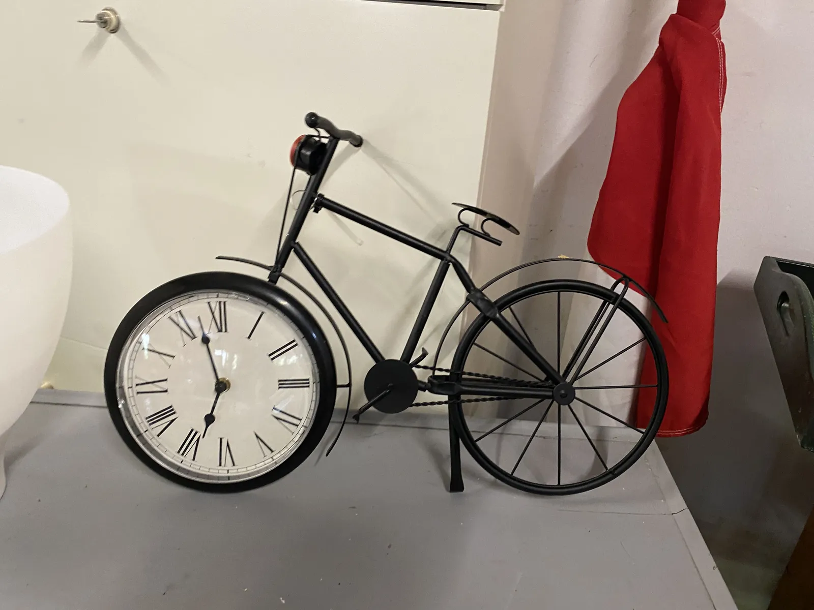 A bicycle shaped clock. The clock is in the front wheel and it points at 3 minutes to seven. The chain of the bicycle is on the right side of the bike, which is very uncommon.  