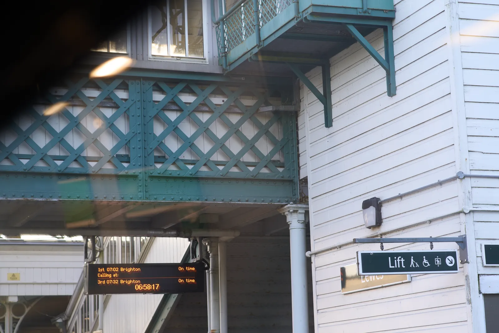 A wooden building with all kinds of balcony-like structures attached to it. A digital display hangs from one of these structures which tells us that the train to Brighton will leave in four minutes. It also says that it is 06:58