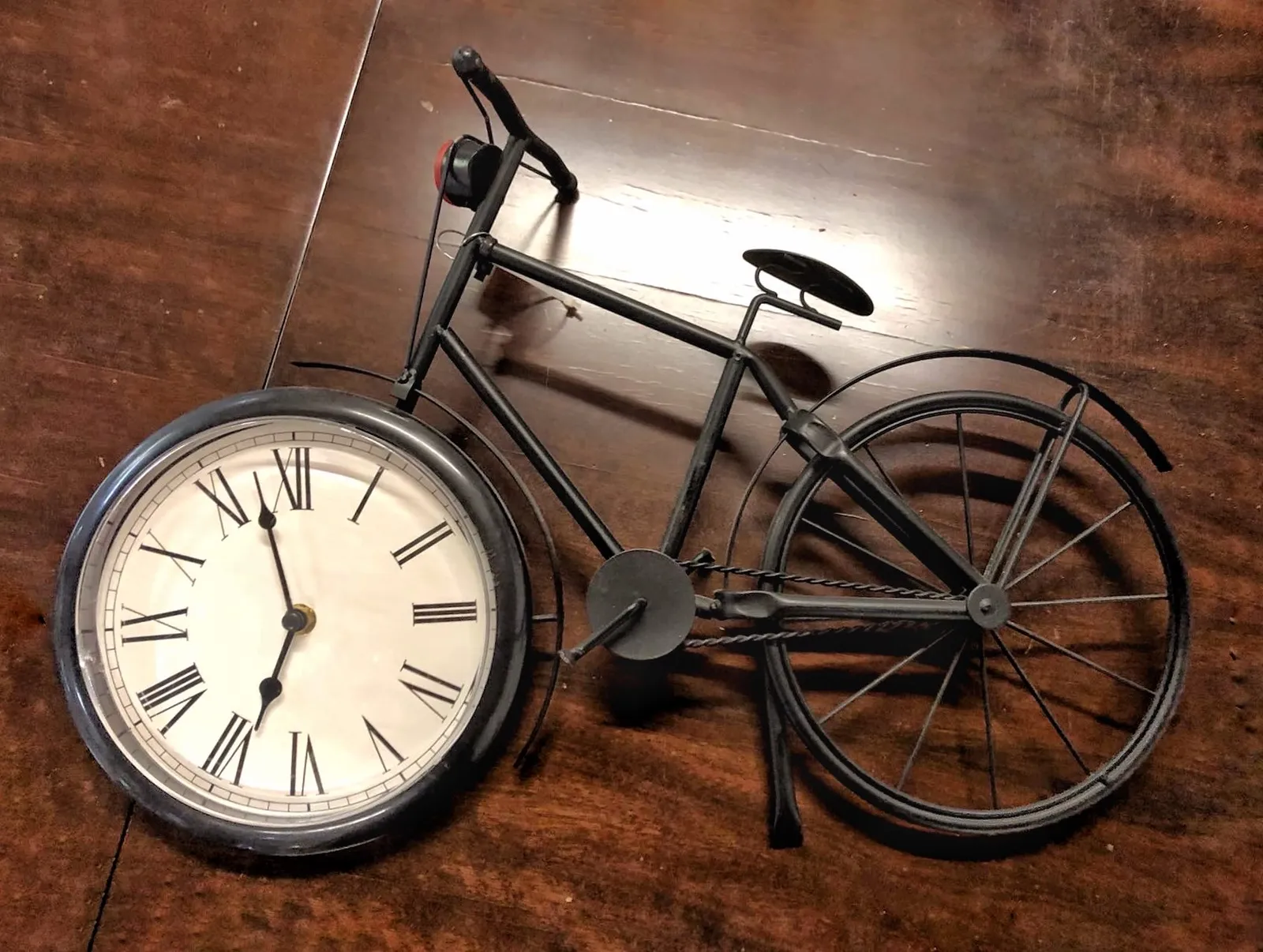 A bicycle shaped clock. The clock is in the front wheel and it points at 2 minutes to seven. The chain of the bicycle is on the right side of the bike, which is very uncommon.  