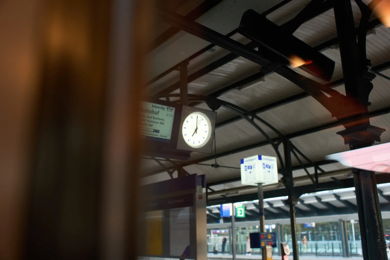 Peeking out from within a train to a clock on the platform. It points at one minute to seven.