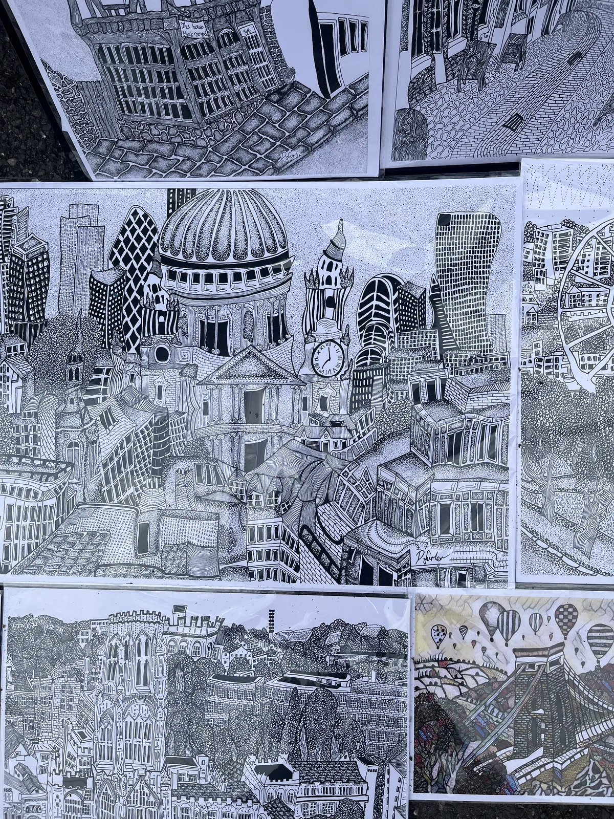 Black and white pen drawings of wobbly buildings. On one of these buildings there’s a clock that points at seven o’clock.