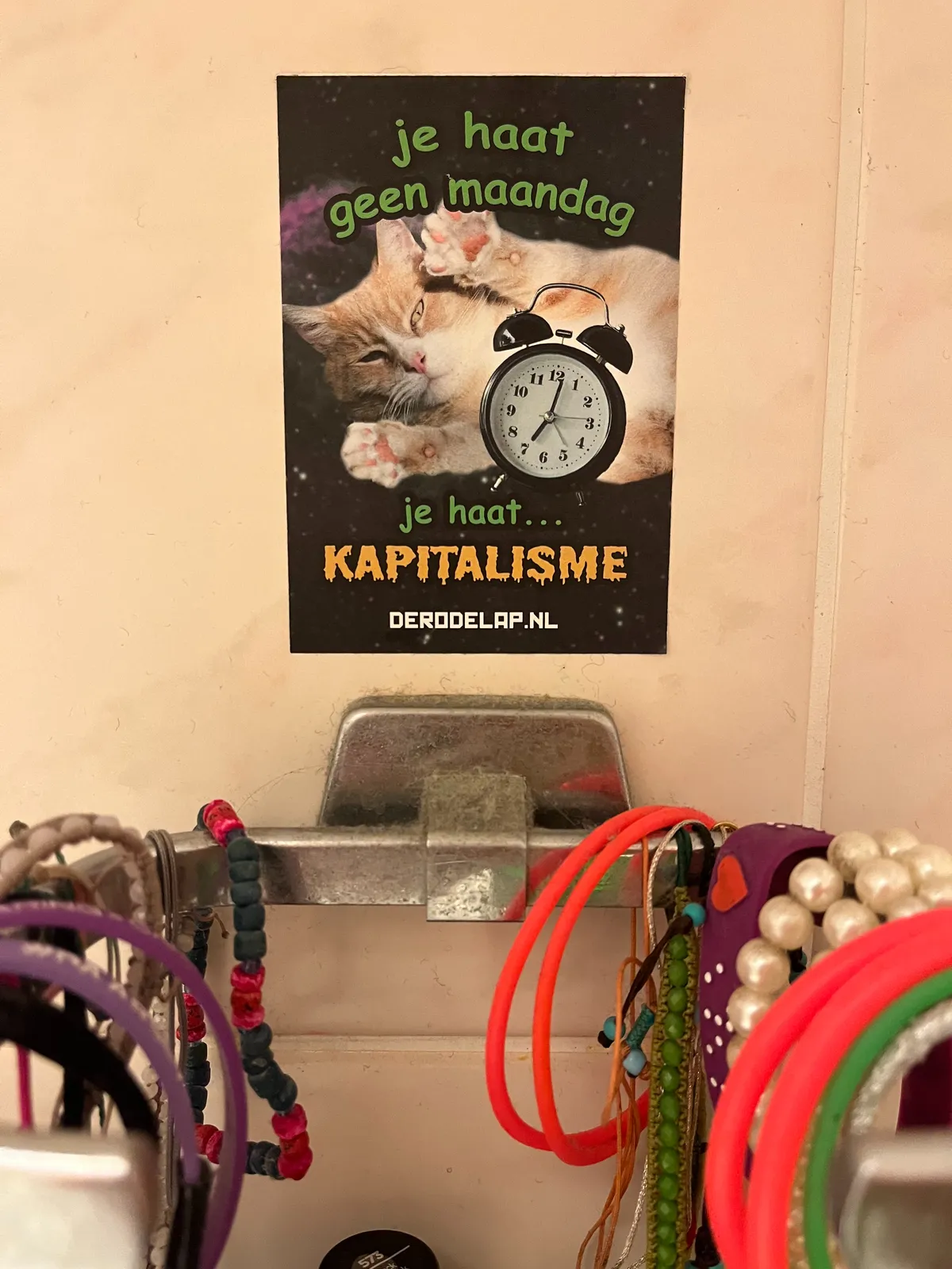 There’s a sticker on a wall, above some colourful elastic bands. On the sticker it says, in Dutch: You don’t hate Mondays, you hate capitalism. There’s also a cat on this sticker and an old fashioned alarm clock that points at one minute past seven.