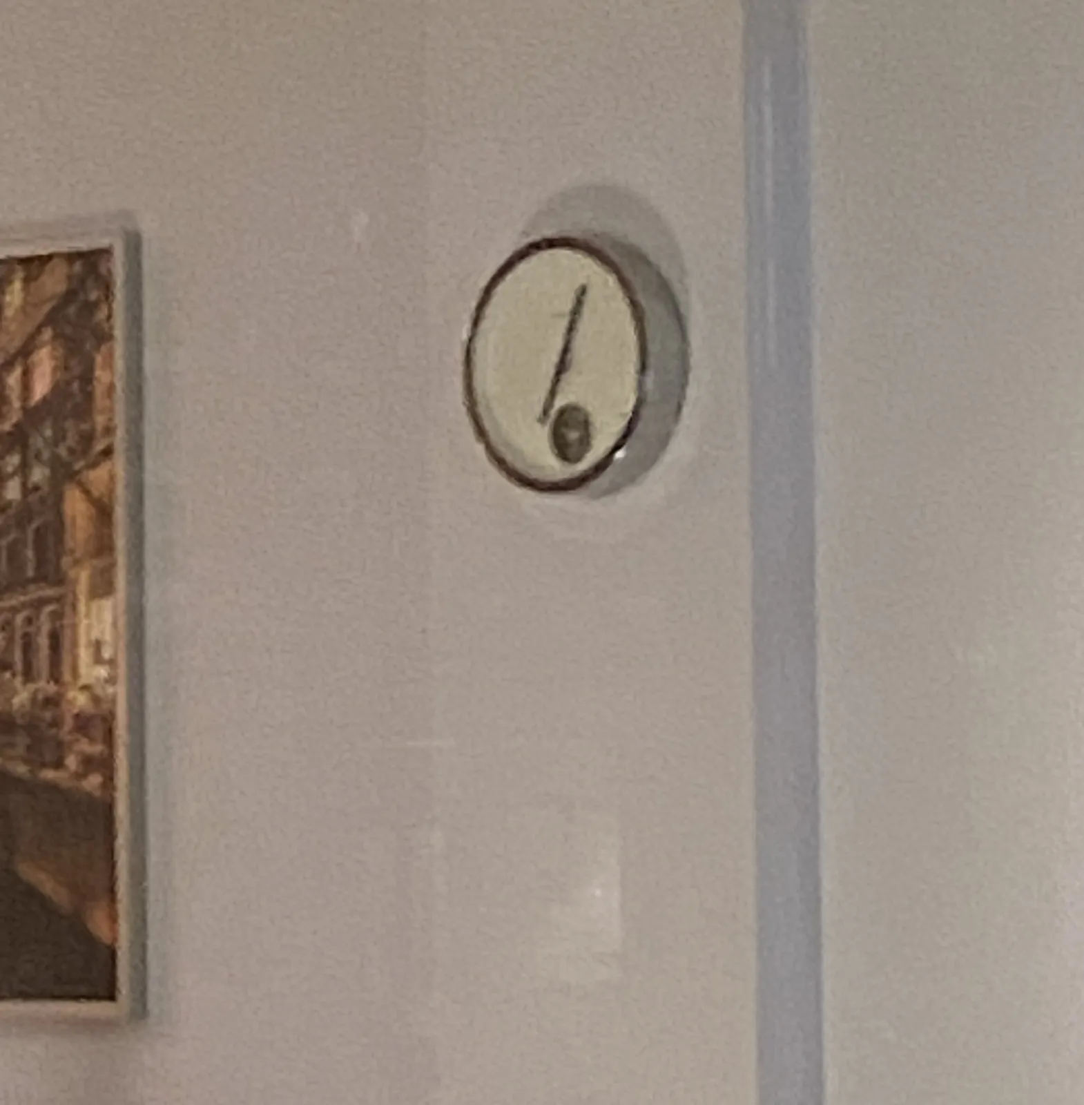 A rather minimalist clock on a white wall. A but blurry. It seems to point at approximately 5 past 7.
