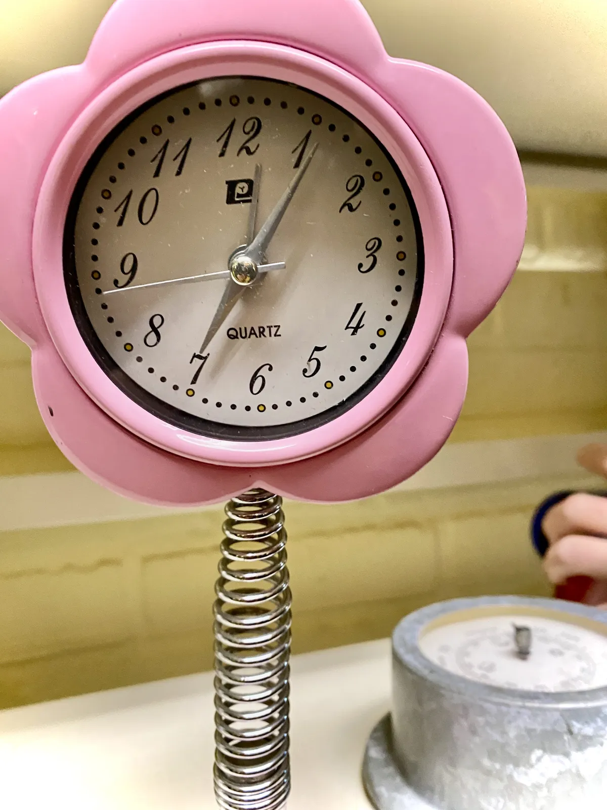 A pink clock on the shape of a flower on a coil spring. It points at 6 past 7.