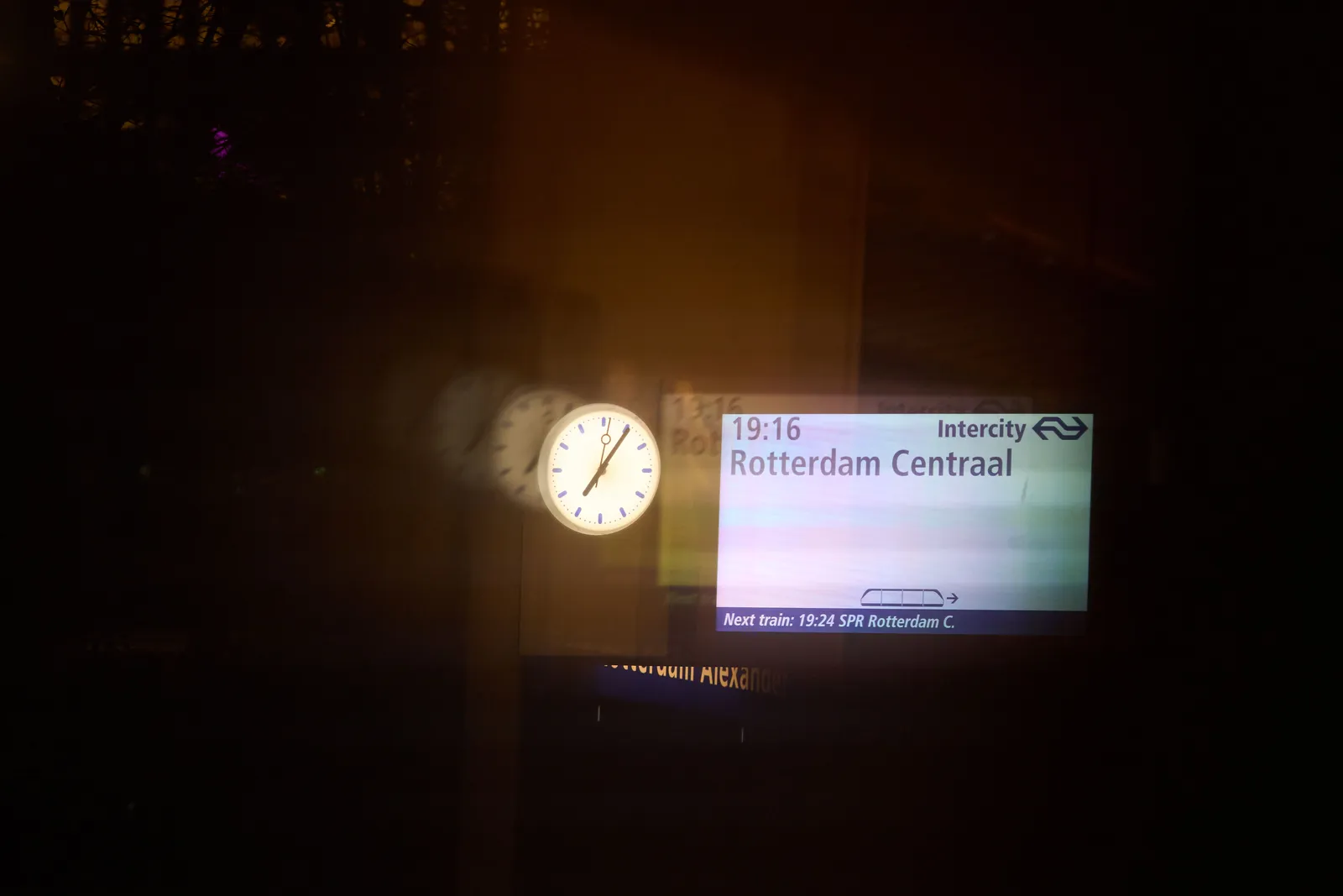 A sign says that the train to Rotterdam will leave at 19:16. According to the clock next to this sign it is 6 minutes past seven.
