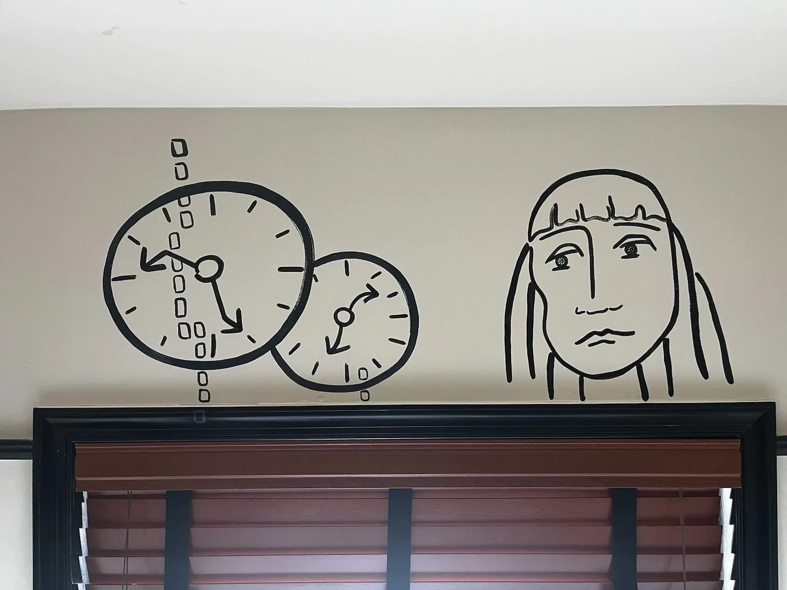 There is a hand drawn face and two hand drawn clocks on this wall. All the hands of both clocks are wavy, or skewed, so assumptions have to be made. One of the clocks may very well point at approximately 14 minutes to six, and the other might point at approximately 9 minutes past 7. One of them is right.