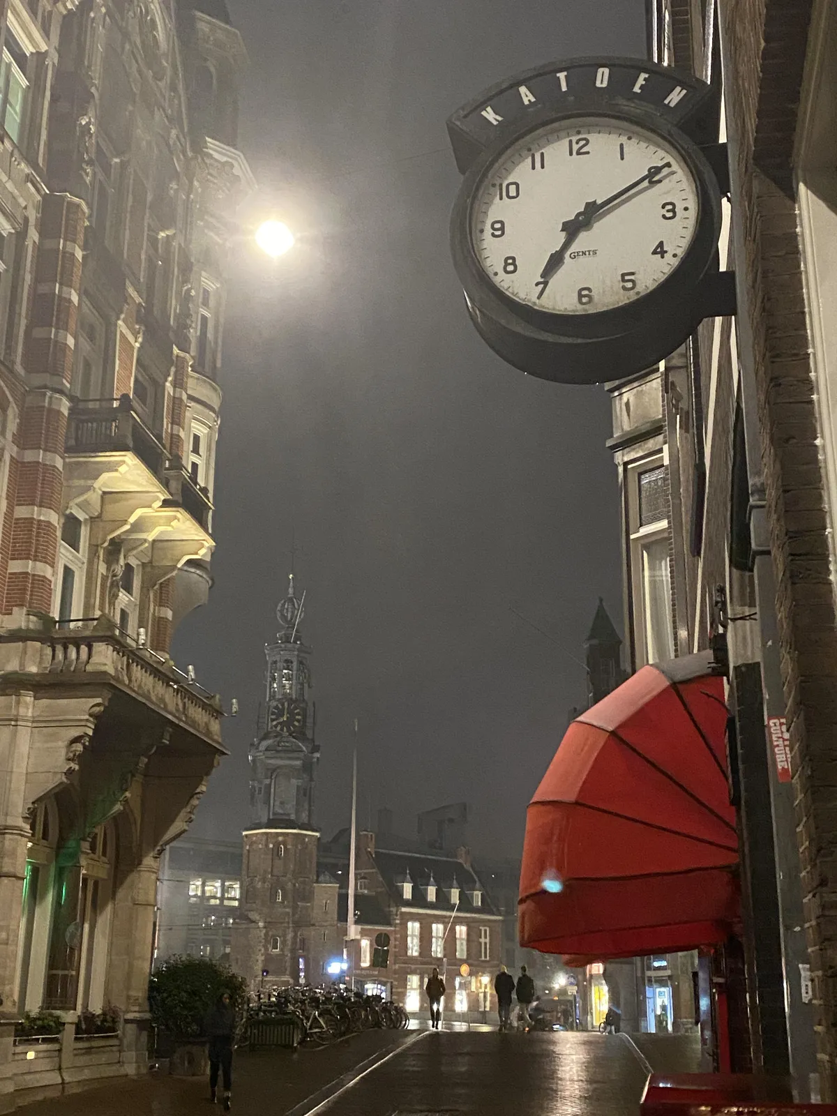 A nice old shopping street in Utrecht, with a square in the background. The word Katoen is displayed over a clock in the foreground. According to this clock it is ten past 7, which it is right now. There’s a clock on a church in the background which points at 8 o’clock.