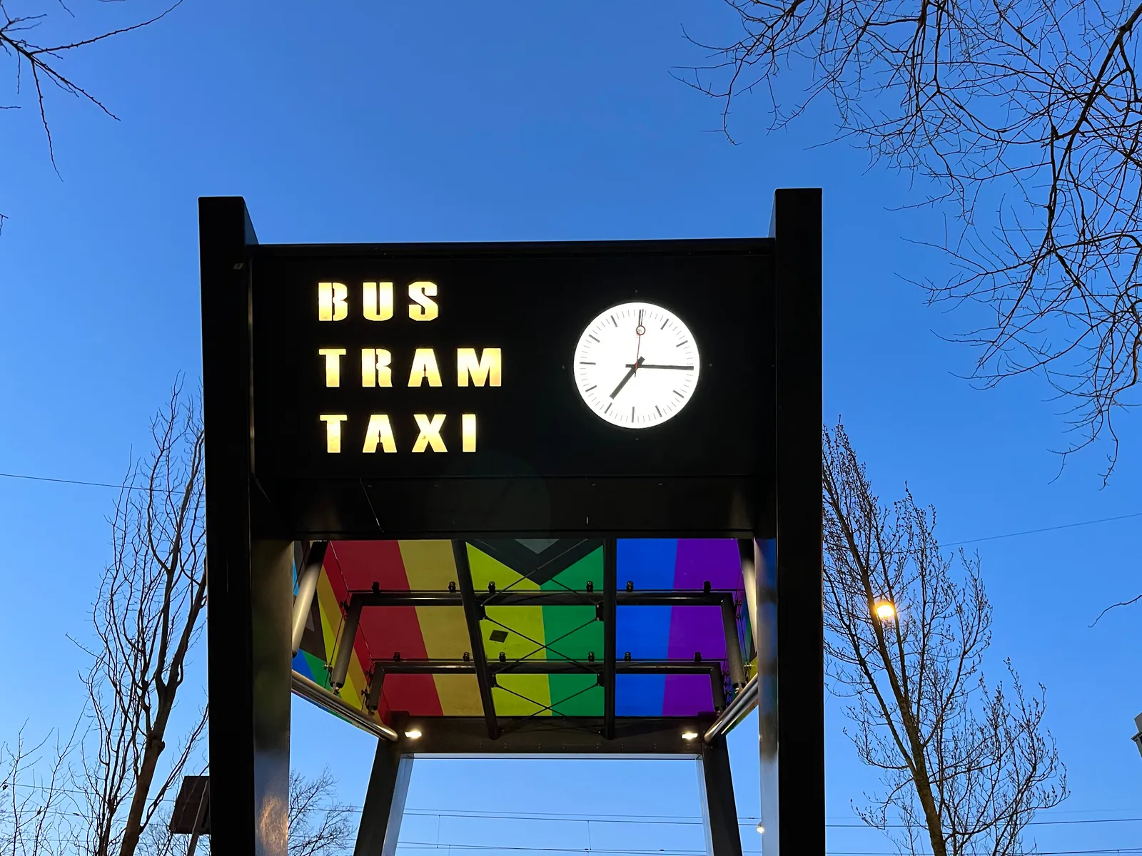 According to this clock on a rainbowy gate to Bus, Tram and Taxi, it is a quarter past 7.