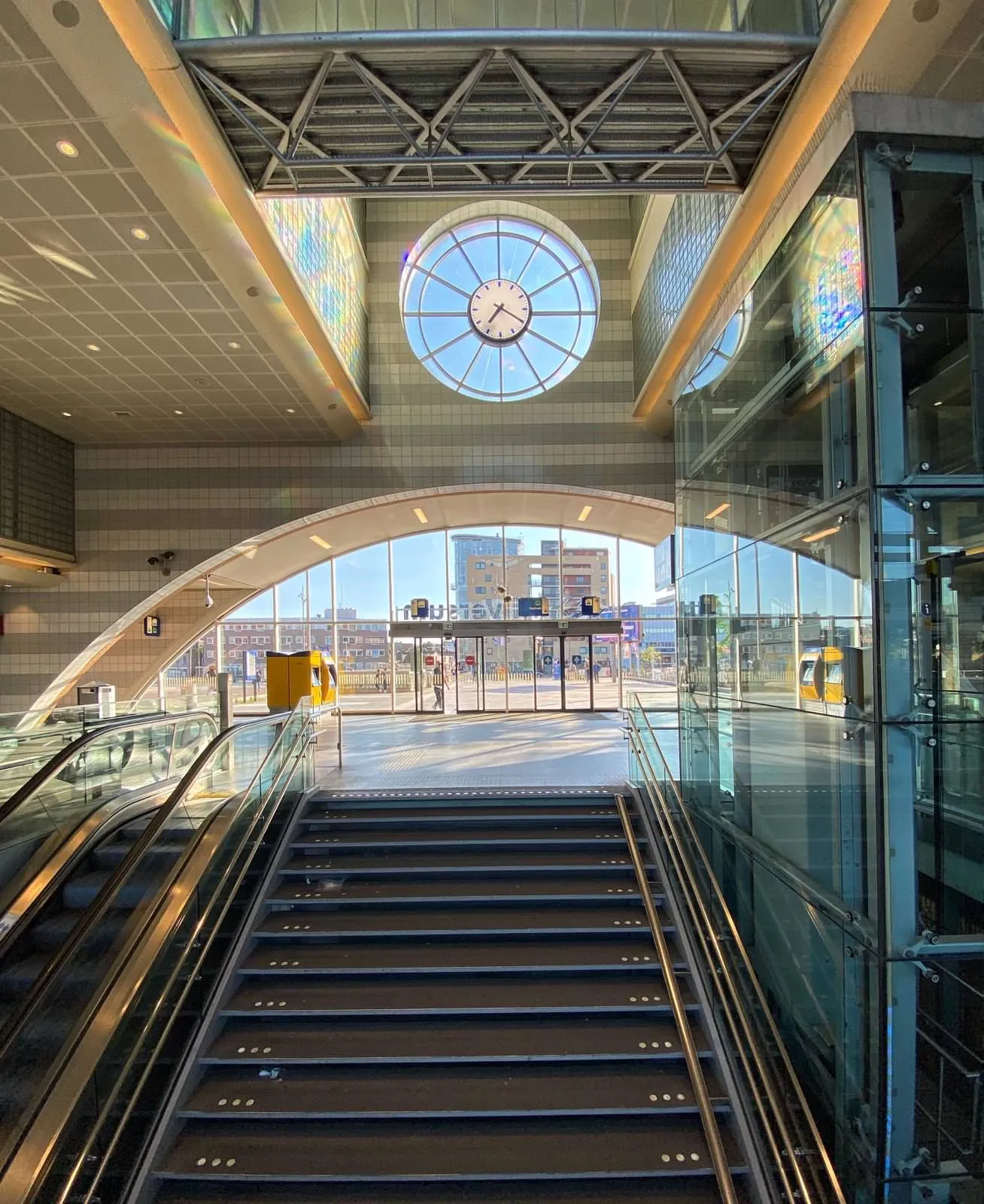 Walking up the stairs in a nicely lit, empty and spacious train station. There’s a clock built into the facade. It points at 20 minutes past 7.