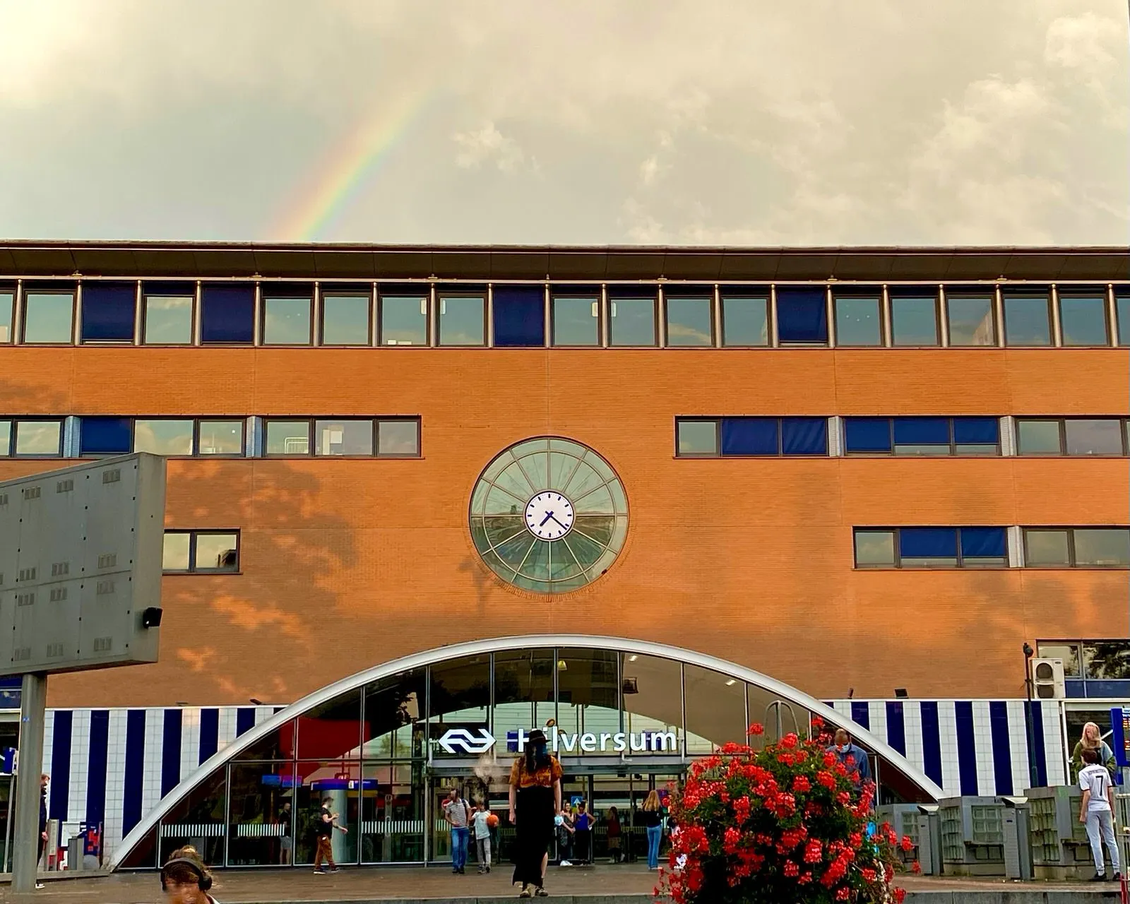 Behind this Hilversum train station there’s a rainbow. On the facade of the station there’s a clock which points at 22 past 7.
