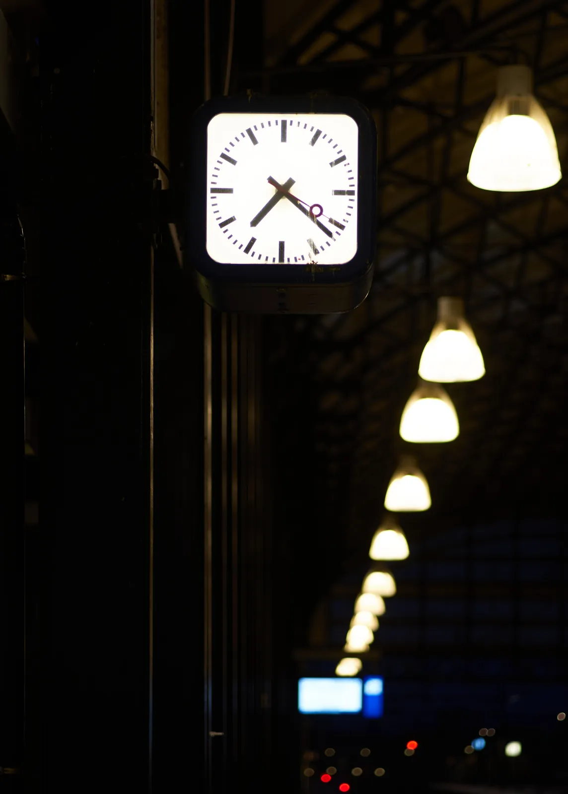 In the background, in the darkness, an array of large industrial lamps. In the foreground there’s this clock that points at 22 past 7. 
