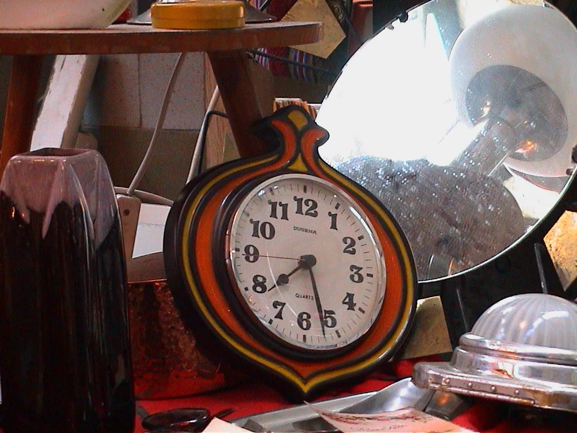 A clock, surrounded by stuff, points at 27 past seven.