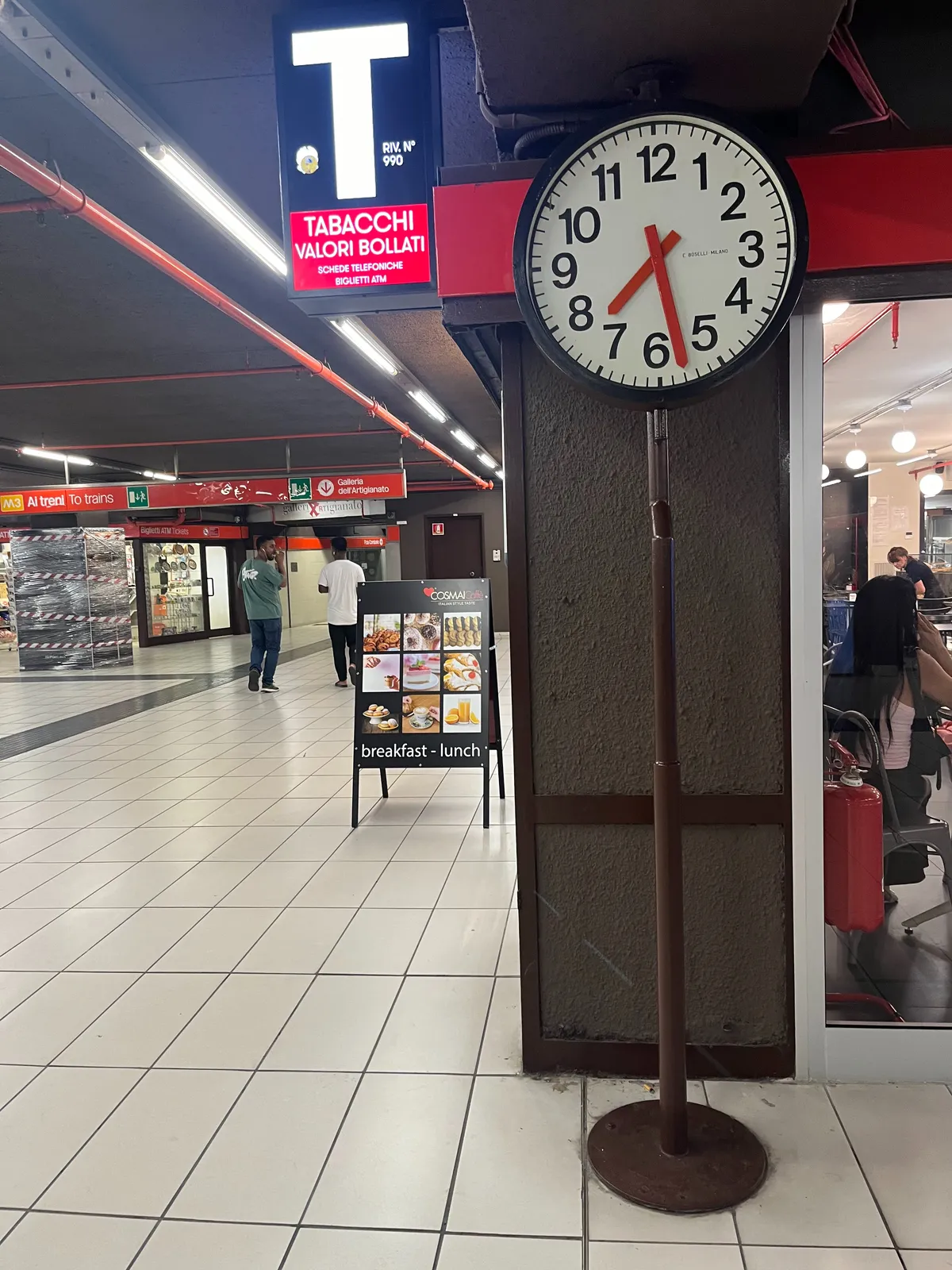In a shopping center in an italian train station there’s a clock in a pole that points at 28 minutes past 7.