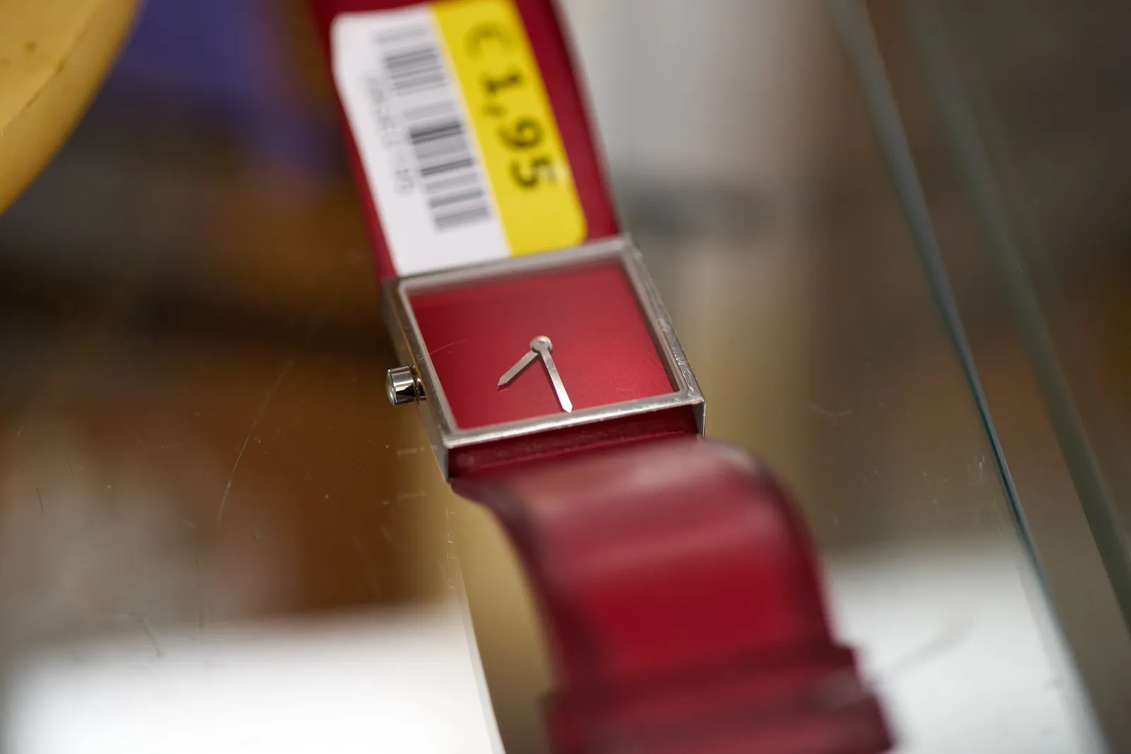 A red, square wrist watch, for sale for just 1,95. It points at 7 thirty.