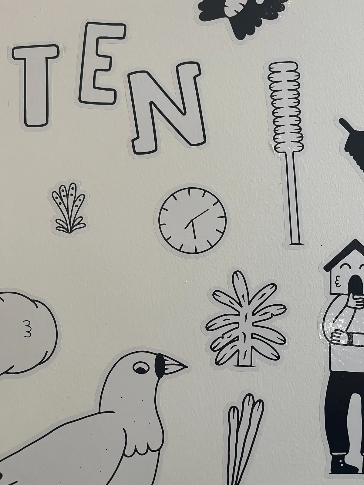 All kinds of happy, black and white stickers on a white wall. One of the stickers is a clock that points at half past seven.