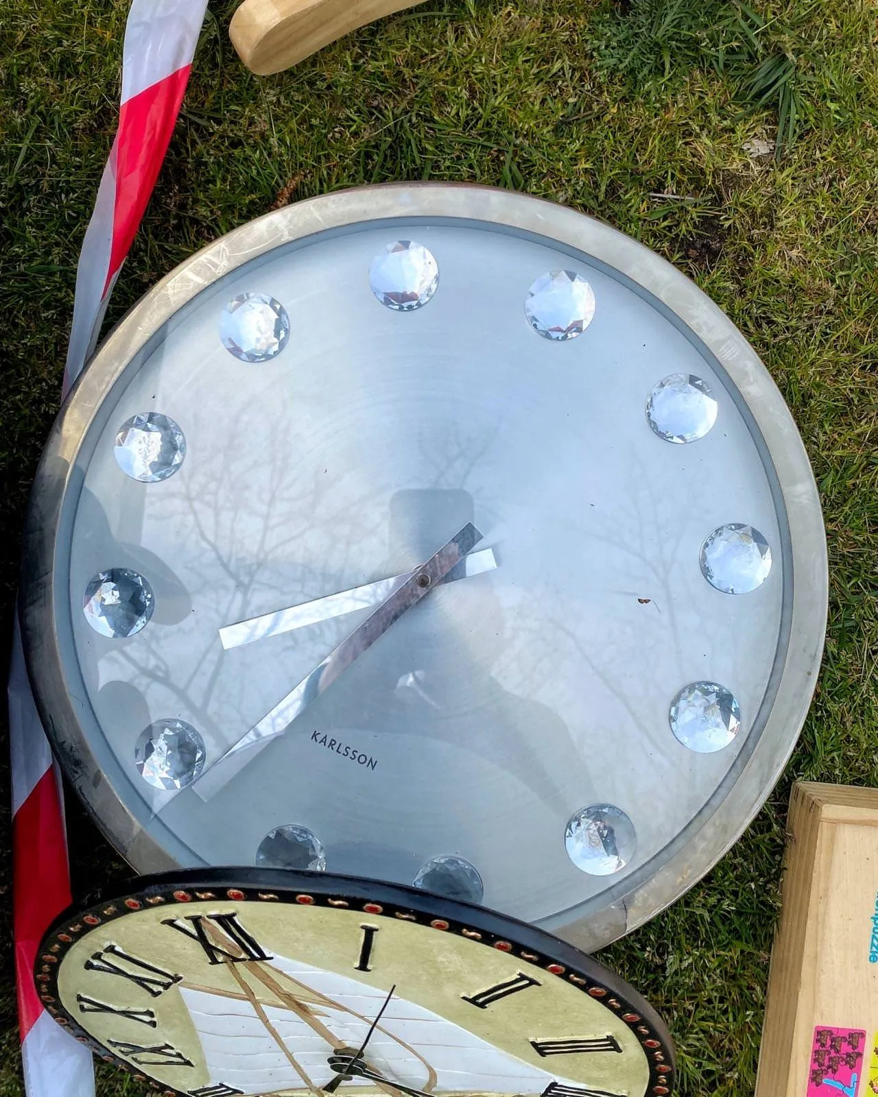 A clock lying on the ground. It’s a bit hard to read since it has no numbers to indicate the time, just diamond like dots. When you assume that the word Karlsson is supposed to be presented horizontally, then it becomes clear that it points at approximately 34 minutes past 7.