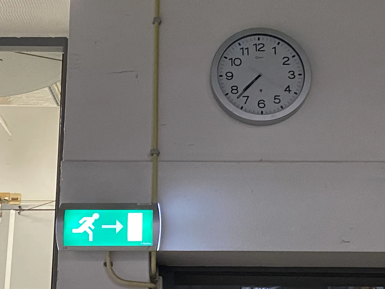 This clock on a wall in an industrial looking environment points at 37 minutes past 7.