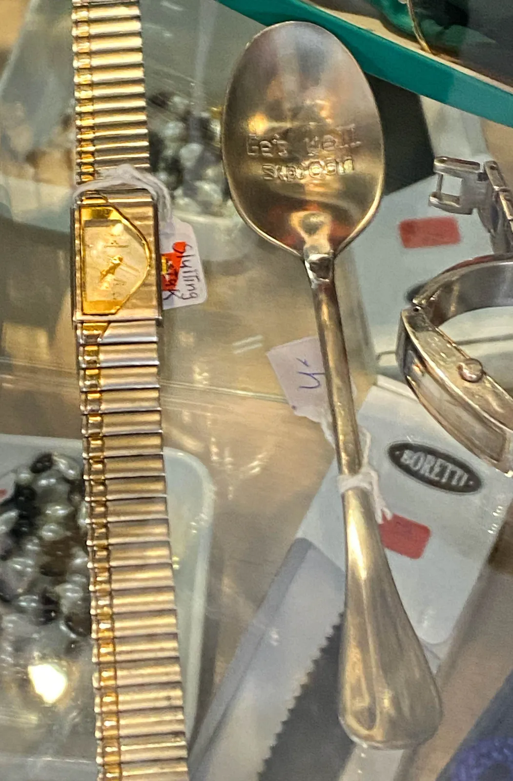 A spoon and a wrist watch. It seems to point at approximately 23 minutes to 7.