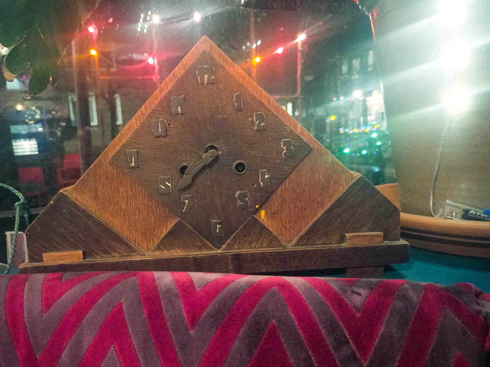 A wooden, triangular clock with a square face on it, and some nicely crafted numerals. It points at 38 minutes past 7.