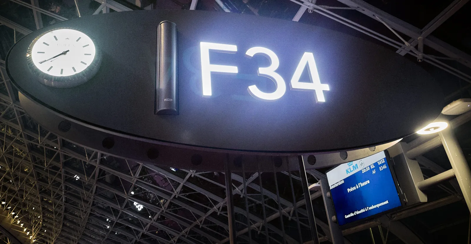 A clock at gate F34, waiting for a flight to Amsterdam. The clock points at 39 minutes past seven.