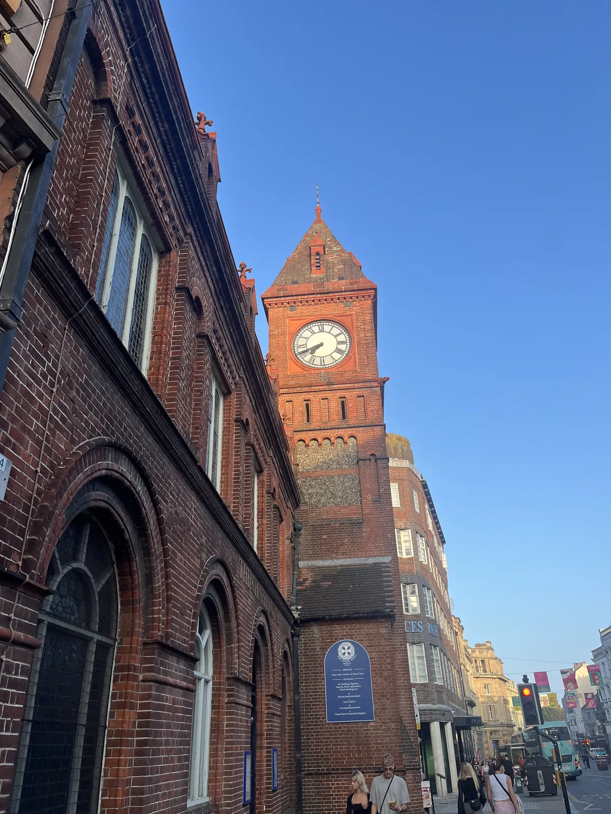 A clock on a brick tower in a shopping street. It points at 19 minutes to eight.