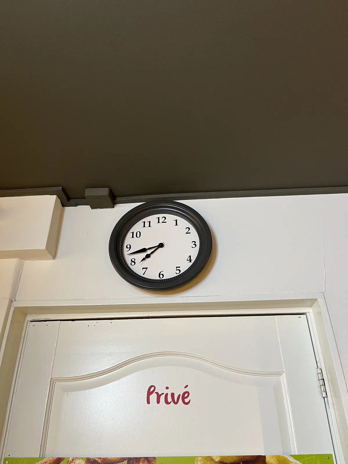 Above a door with the word Privé painted on it, there’s a clock that points  at 17 minutes to eight.