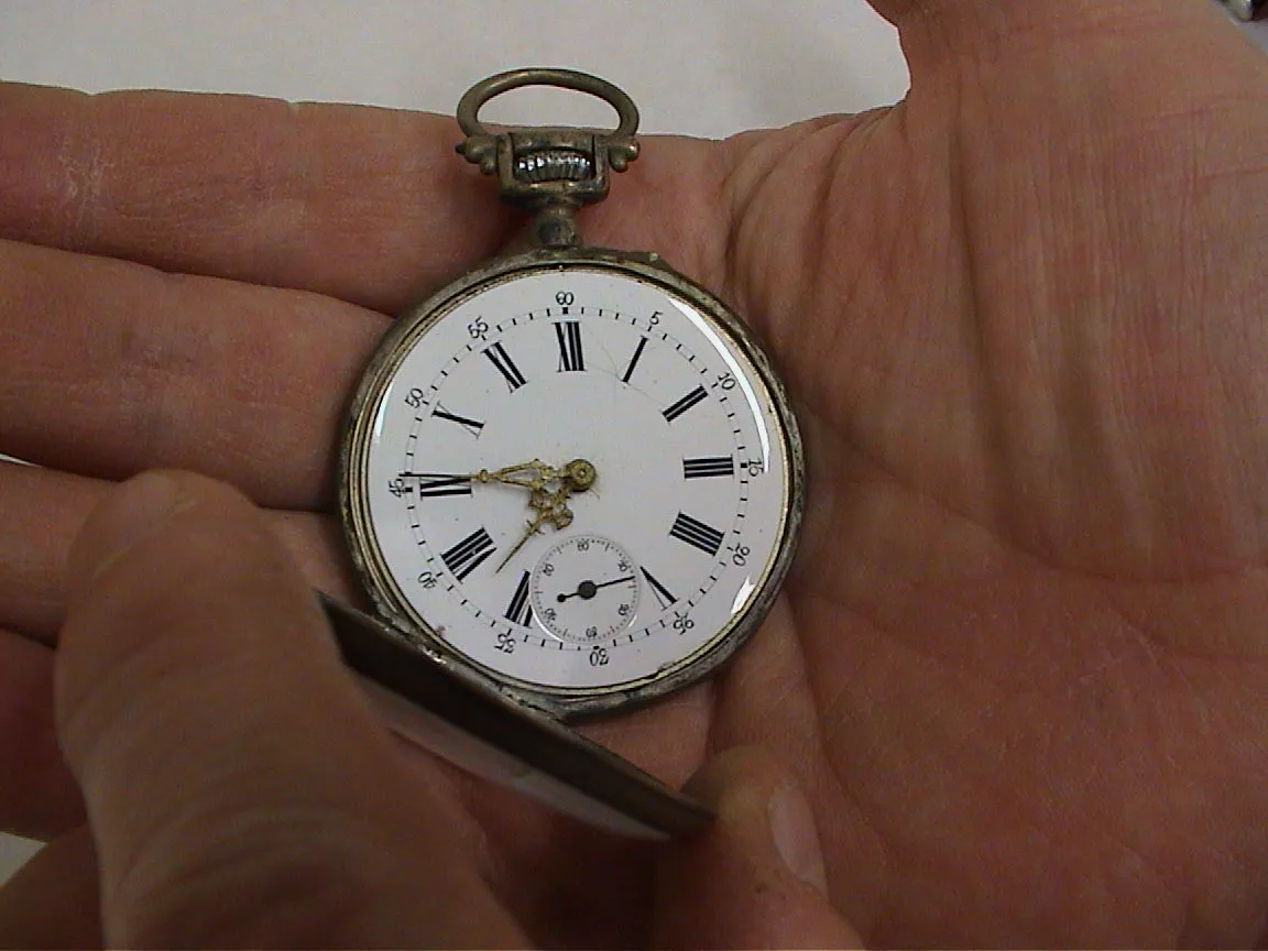 This old watch (without a chain) points at fourteen minutes to eight. It is held in a hand.