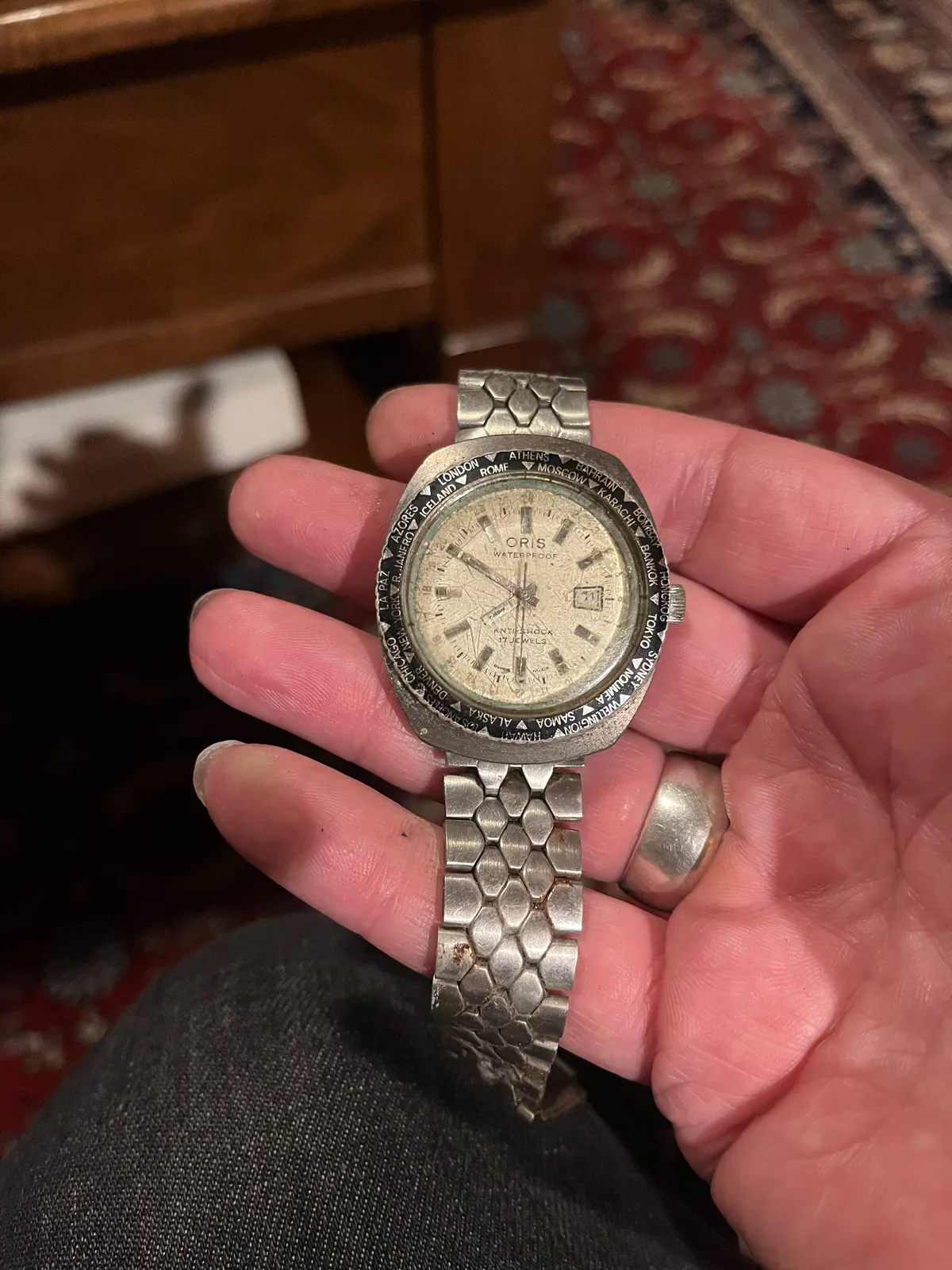 Someone is holding an old watch in their hand. In the background, blurry, an old Persian rug. The watch points at 10 to eight.