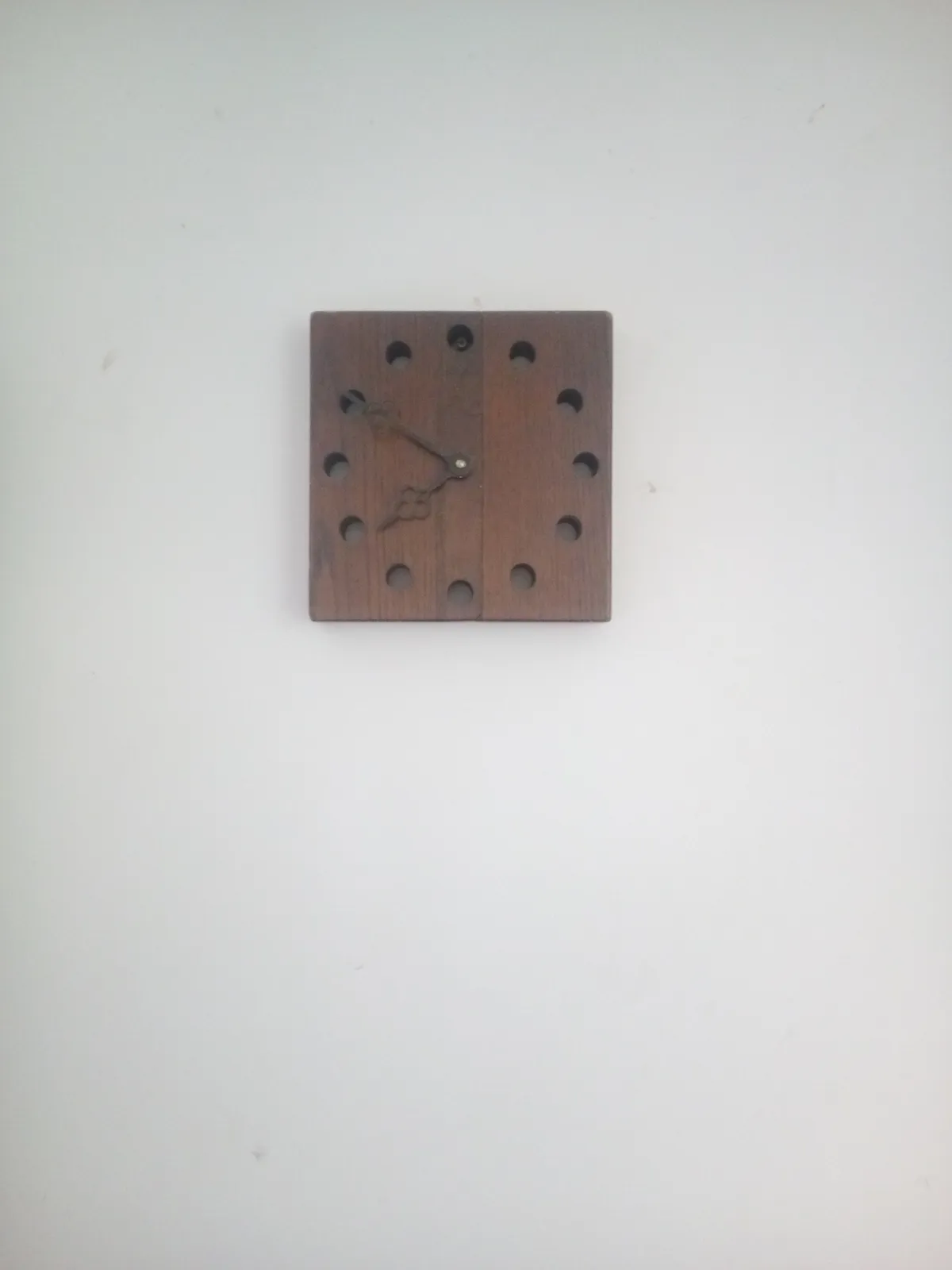 A wall clock made from wood, with holes drilled in it. It points at 10 minutes to eight.
