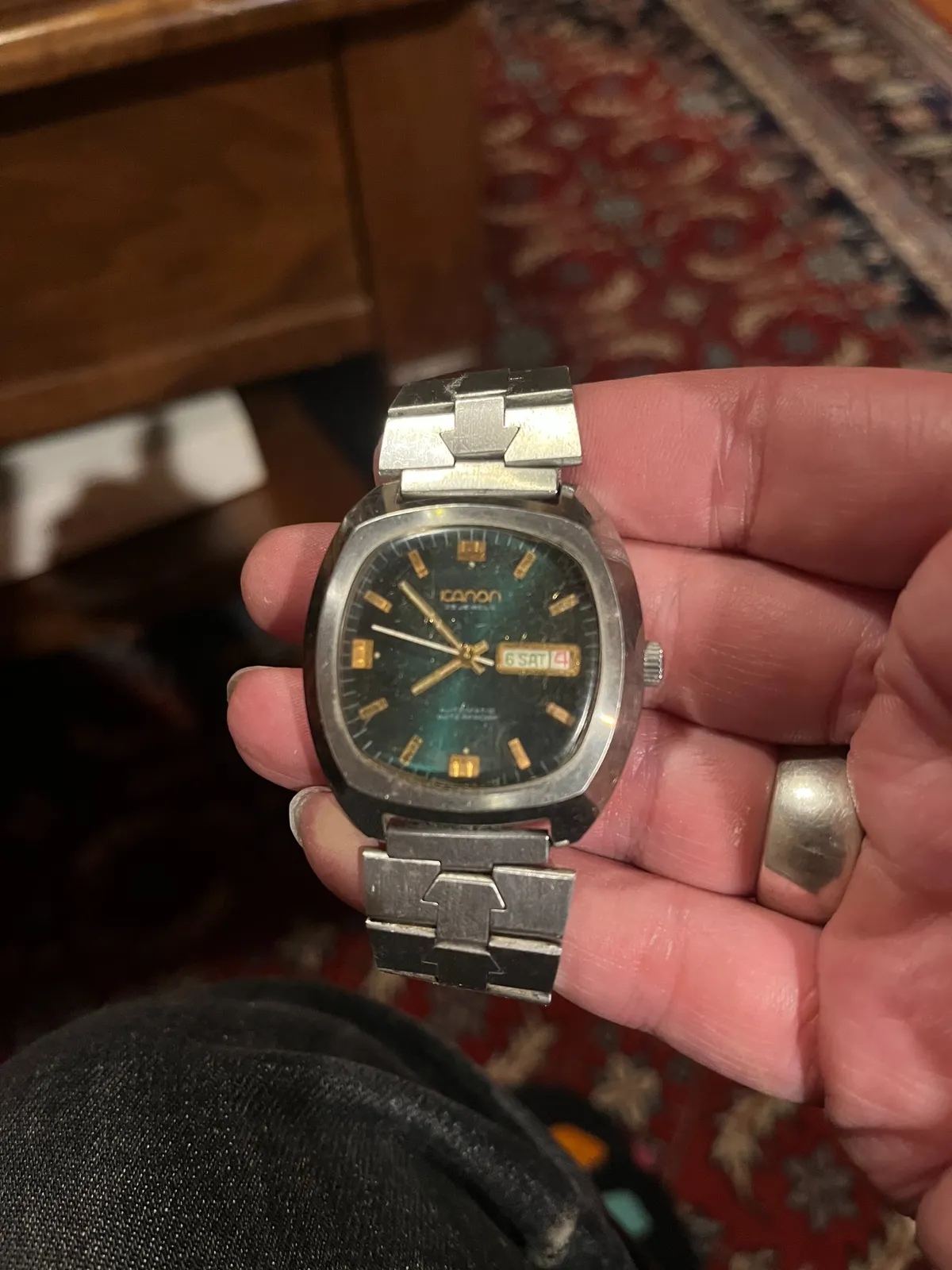 Someone is holding an old watch in their hand. In the background, blurry, an old Persian rug. The watch points at 8 minutes to eight.