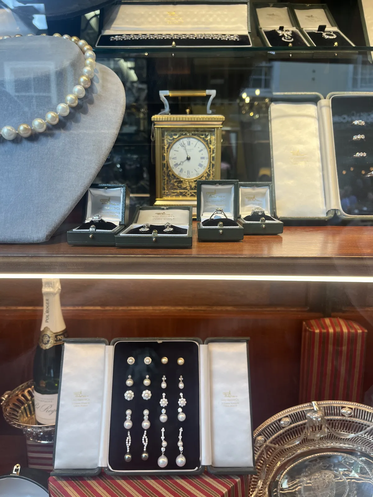Luxurious jewellery in a shopping window, with a bottle of champaign, and a golden table clock. The clock points at 8 minutes to eight.