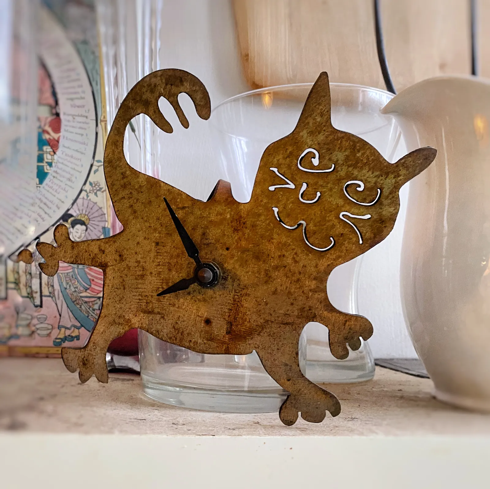 A clock made from a sheet of metal, cut in the shape of a cat. The clock points at approximately 8 minutes to 8.