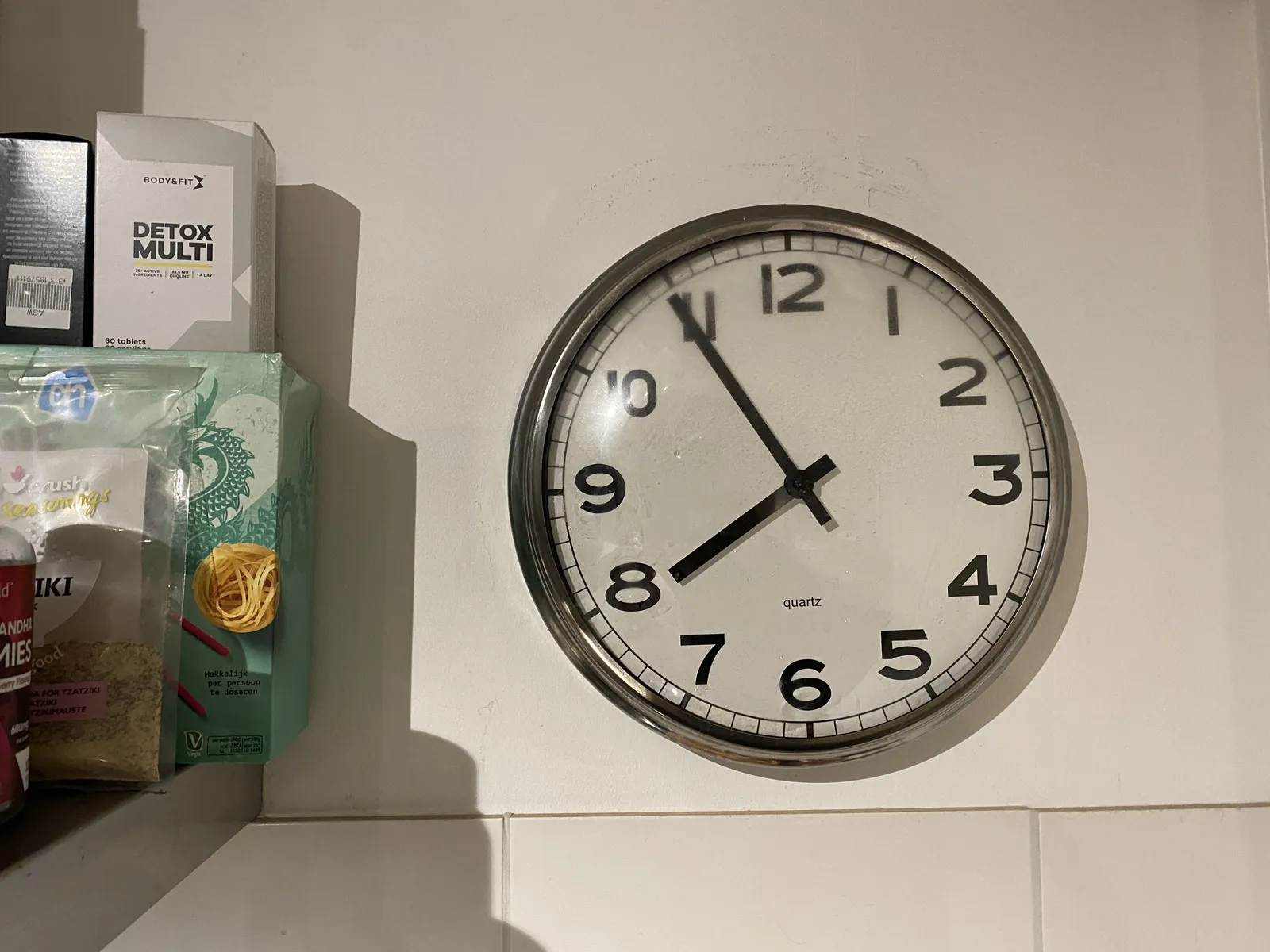A wall clock, next to some boxes of food, points at 6 minutes to 8. 
