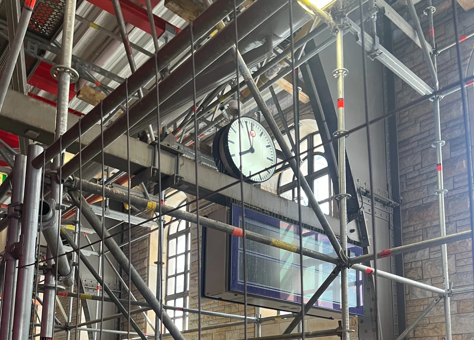 A station clock surrounded by scaffolding. It points at 2 minutes to 8.