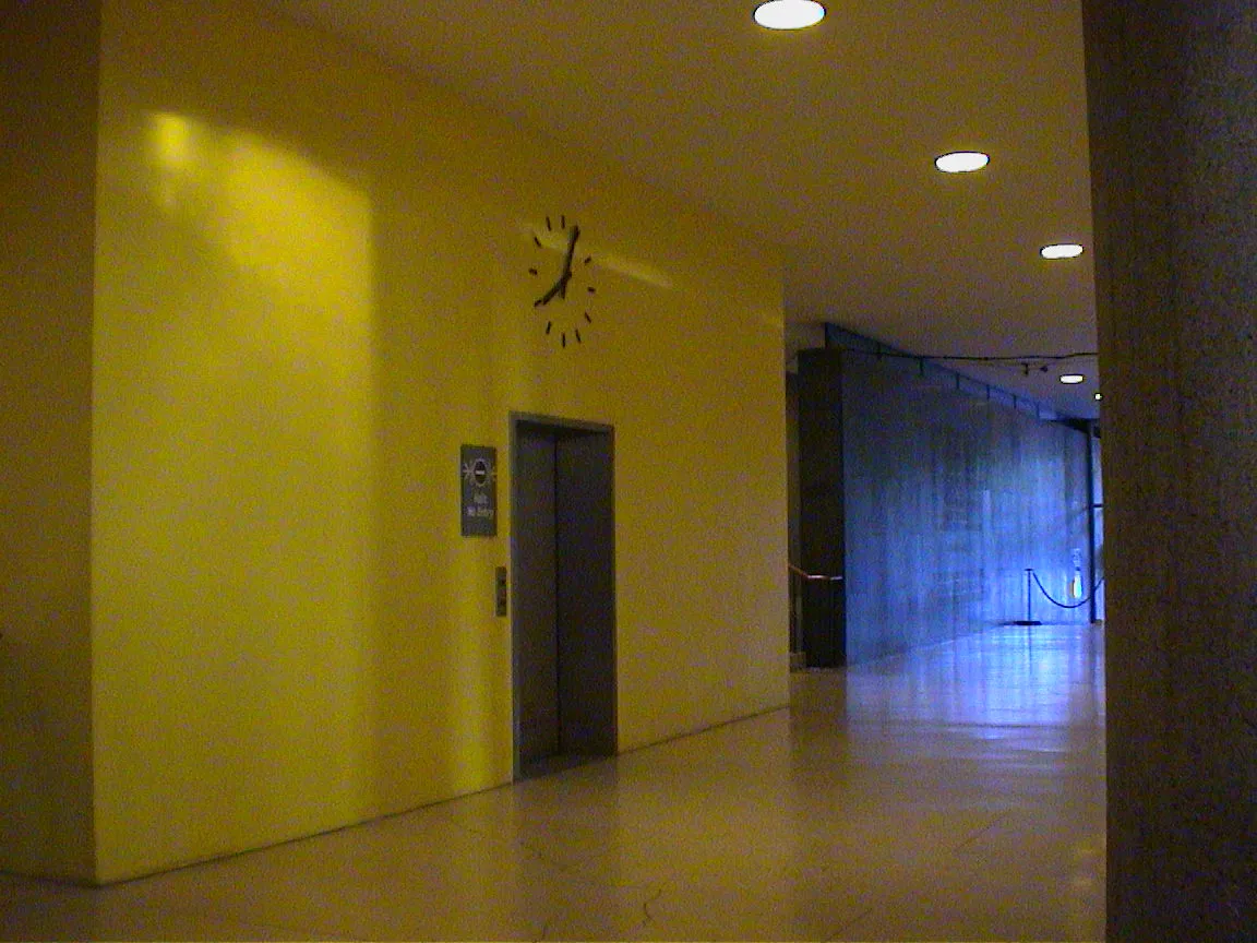 This is a clock that’s built into a wall, above an elevator. The hour arm is a bit off, but it seems like it points at four past eight.