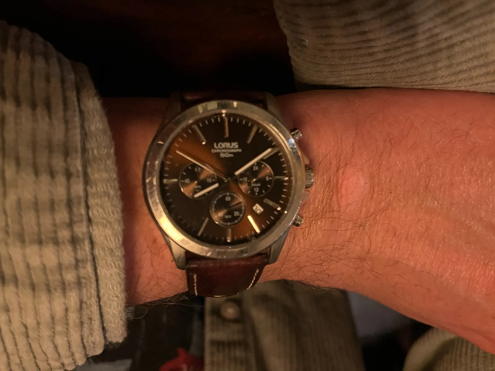 Someone’s wrist with a wrist watch. The moniker Lorus is printed on the clock’s face. It points at 9 minutes past 8.