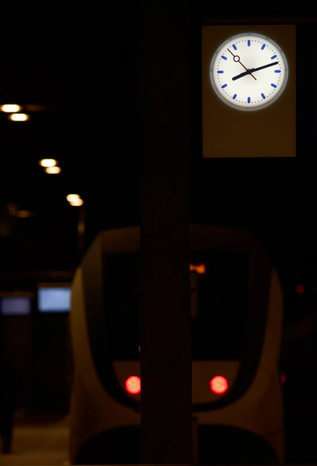 Blurry in the background there’s a train. In focus there’s a clock that points at 12 past 8.