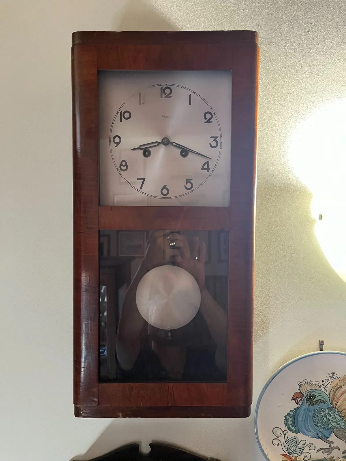 An old wooden clock that points at 18 minutes past 8. The hands of the photographer can be seen, mirrored in the glass cover.