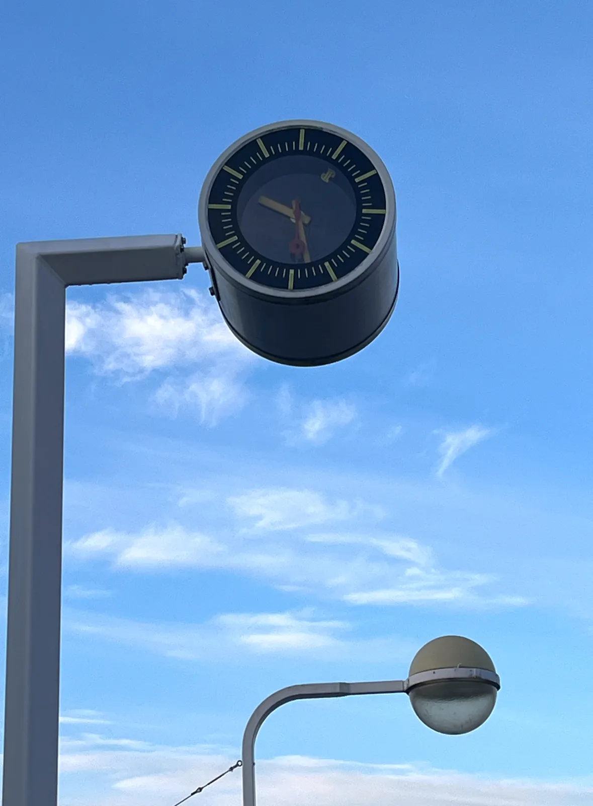 A blue sky with a few thin, small clouds. A bulbous lamp on a pole in the back, and a clock in the front. It seems to point at 27 minutes past nine. If you look very close you can see that the clock is in fact not upright! It is rotated 30 degrees. So it could also be 22 minutes past 8.