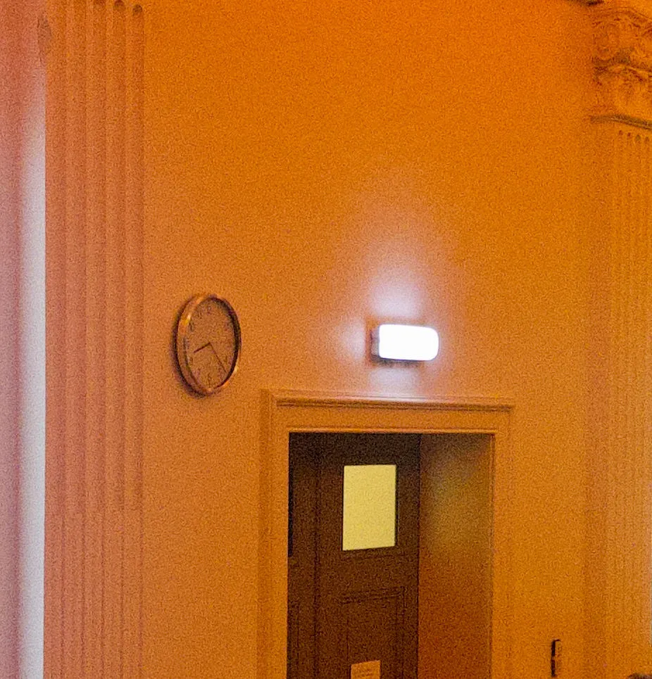 A clock next to the exit sign above a door. It’s between two neo-classical columns. The clock points at 23 minutes past 8.