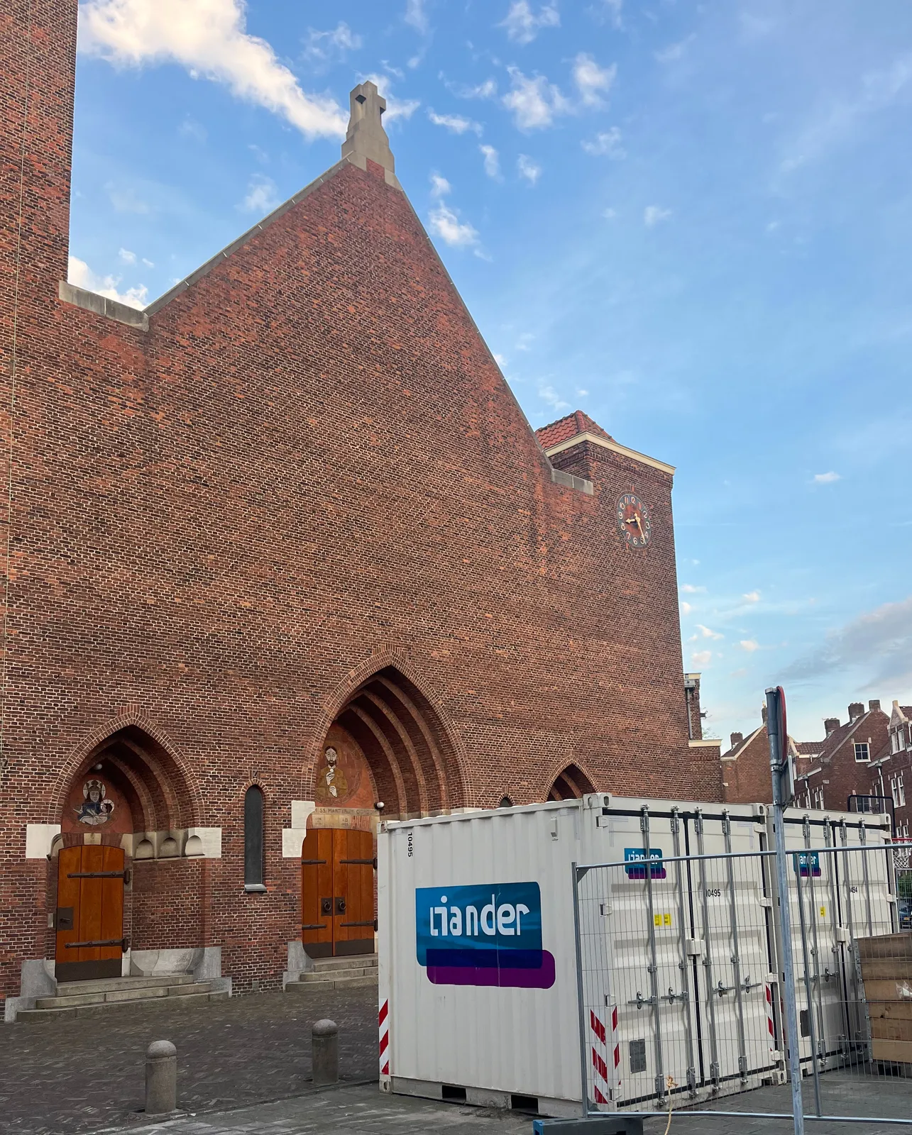 A monumental brick church with a clock built into its facade. There’s a gray container standing in front of the church. The clock points at 24 minutes past 8.