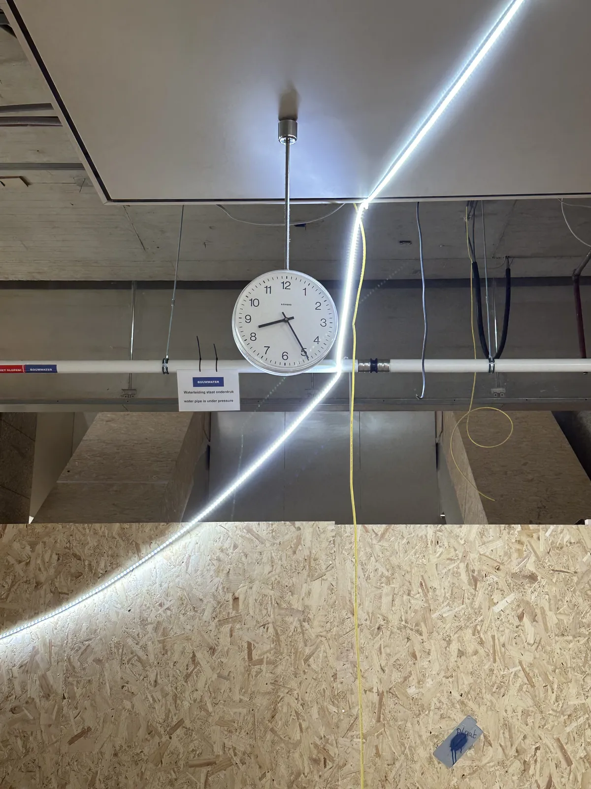 A clock hanging from a ceiling, right in the middle of a construction site. The clock points at 25 minutes past 8.